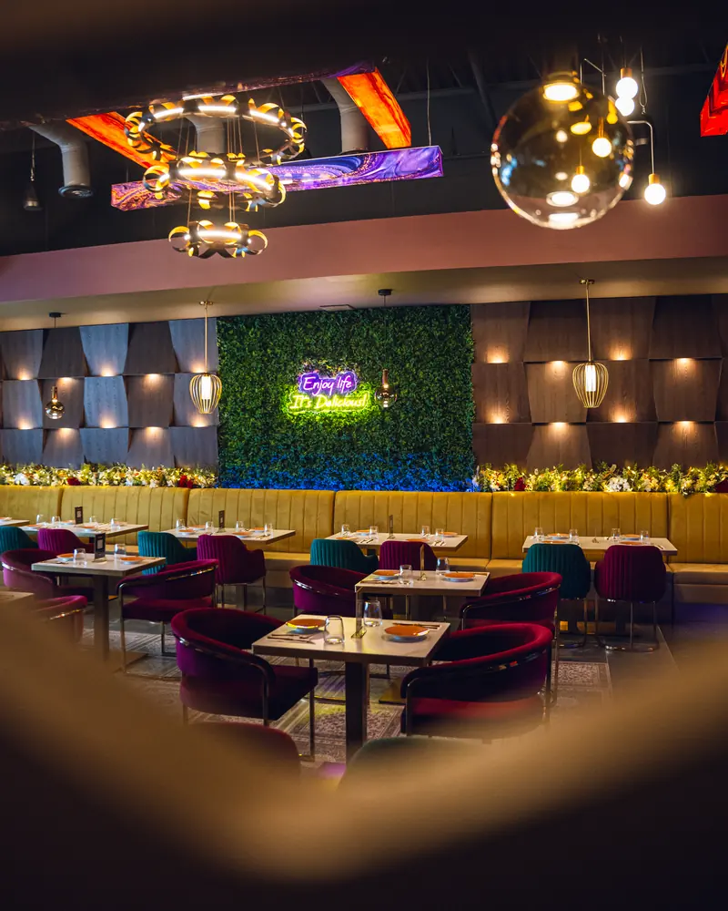 A long banquette running beneath the living green wall and its neon sign