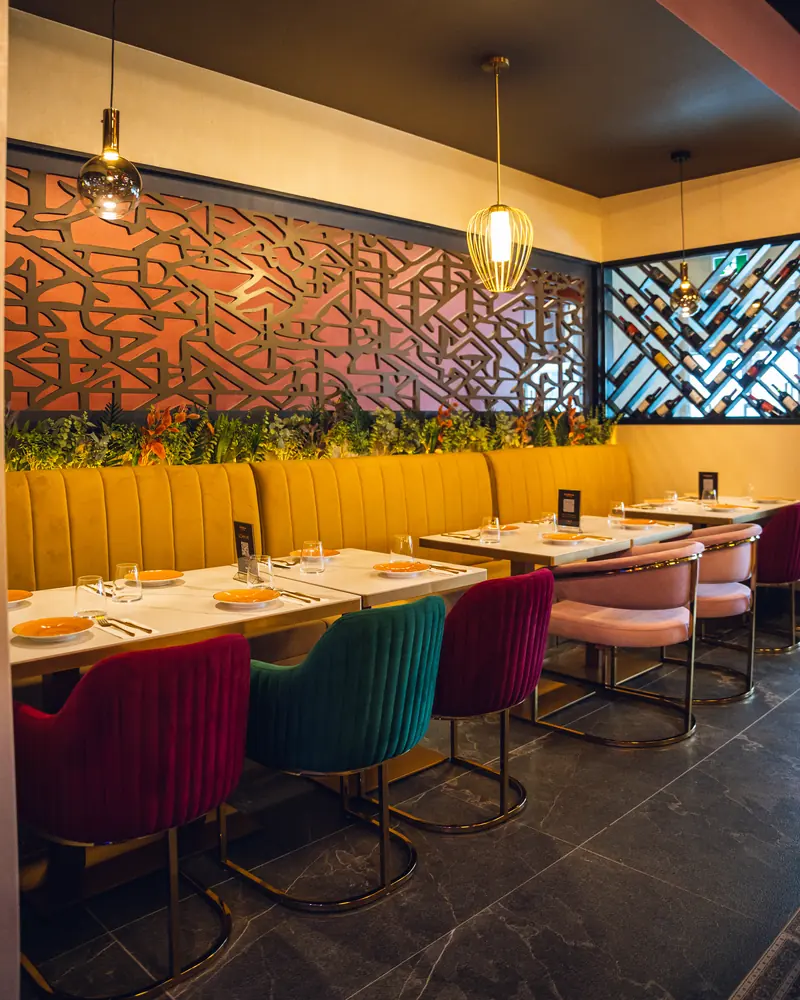 Banquette seating in front of a carved screen wall, under brass pendant lights