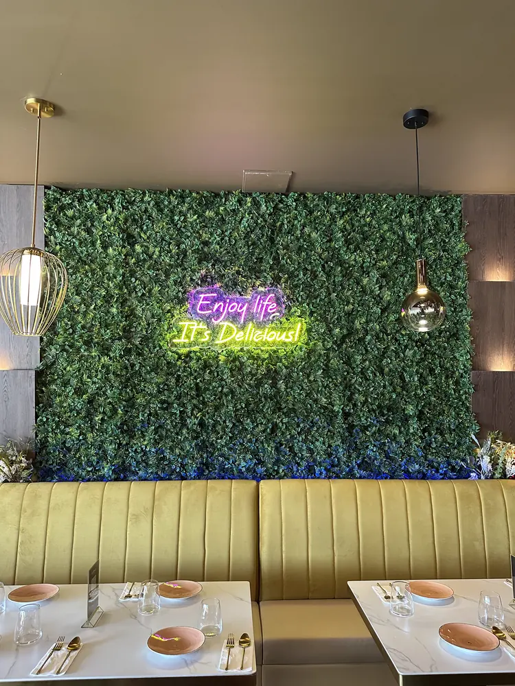 The living green wall straight on, with the neon sign glowing above the banquette